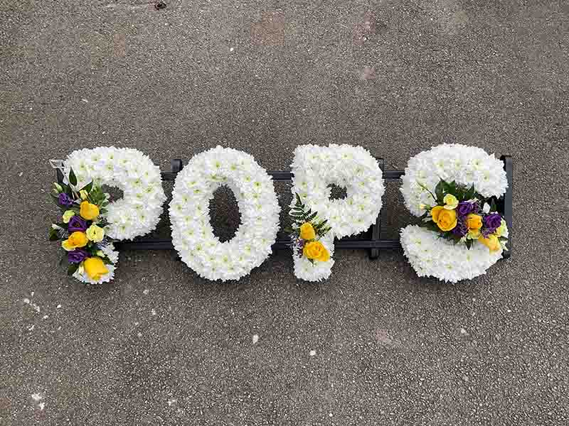 White yellow and purple funeral flower writing spelling out pops
